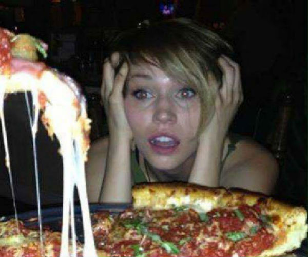 Girl looking at a piece of pizza as melted cheese falls off of it