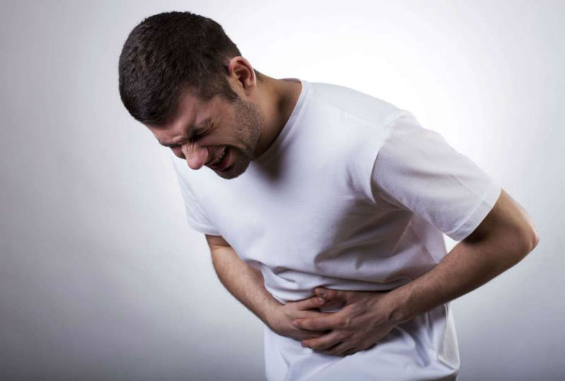 man with sports hernia abdominal pain tenses in pain as he uses his arms for support