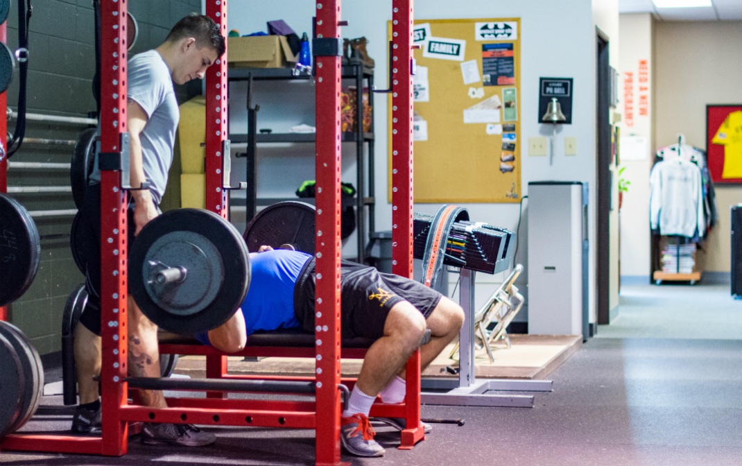 Spotter helps lifter perform a bench press pyramid program to increase strength