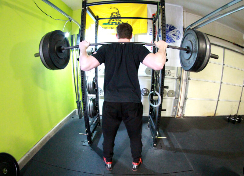 Man performs low-bar barbell squats in physiqz gym following an advanced powerlifting program designed for maximal strength and muscle