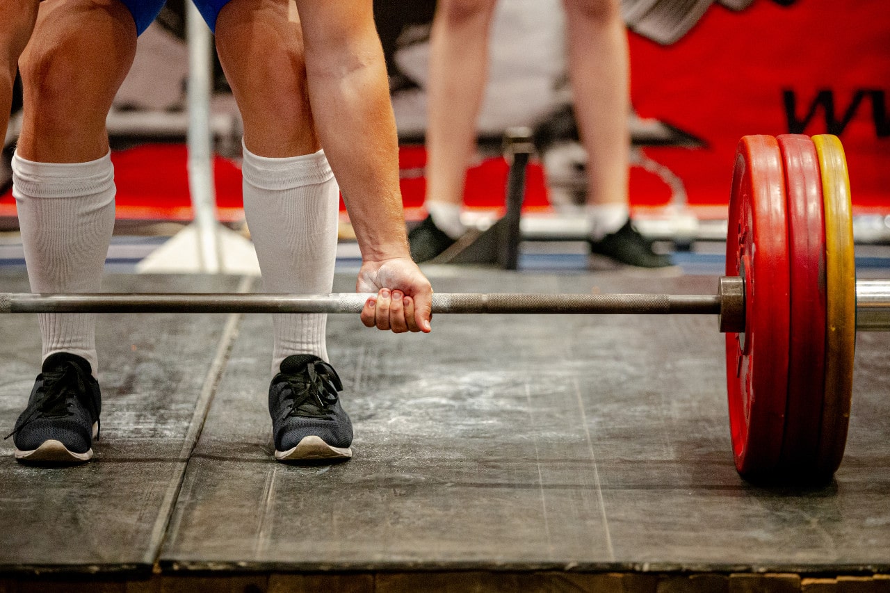 Man sets up to perform deadlift using underhand grip in a gym. This weightlifting exercise is involved in competitions where cutting water weight can help lifters acheive specific weigh in goals.