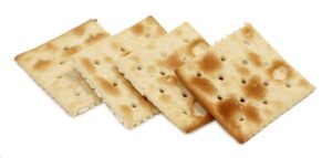 A stack of premium saltine crackers with salt on the surface.