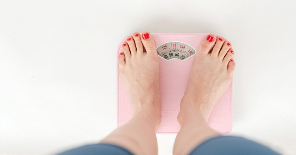 A woman is standing on a scale after trying to get rid of belly fat through diet and exercise. 