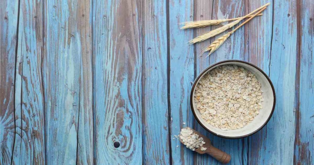 Half a cup of oatmeal on a table alongside rolled oats.