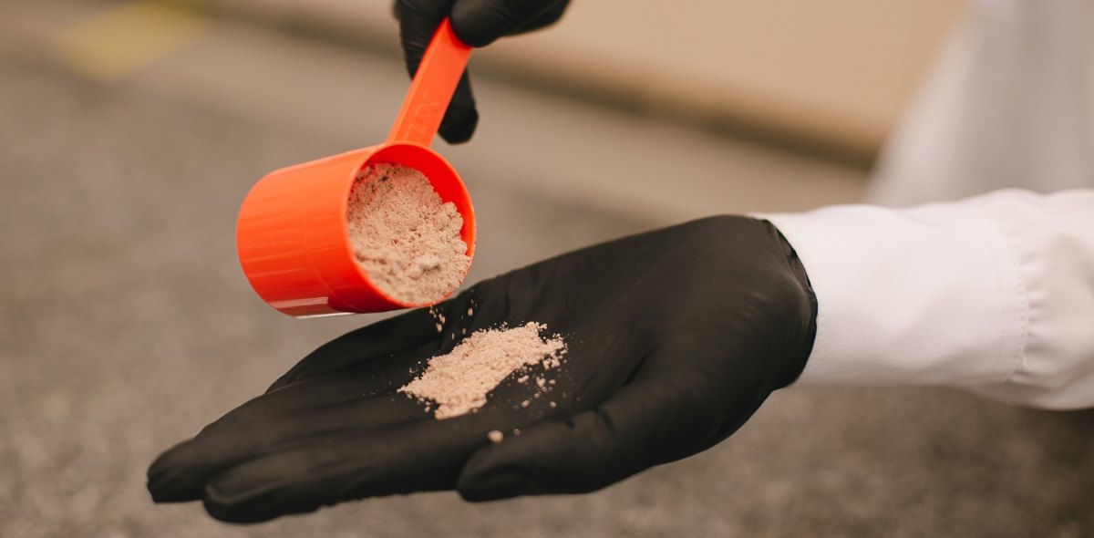 A person examines a sample of Herbalife protein powder by pouring a scoop into their hand.