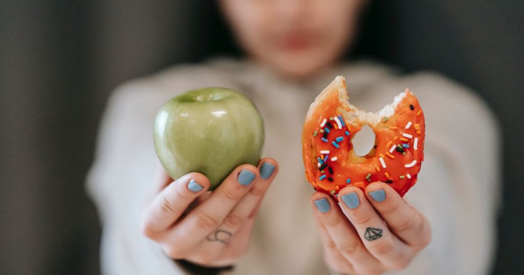 A woman is holding up an apple and a donut to symbolize substituting junk food for healthier alternatives. 