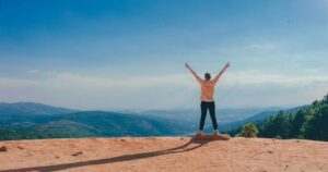 A woman standing at the top of a mountain with her arms spread wide since she conquered her weight loss goals using affirmations for motivation.