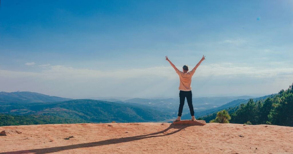 A woman stands at the top of a mountain, arms spread wide, celebrating her weight loss success achieved through motivational affirmations.