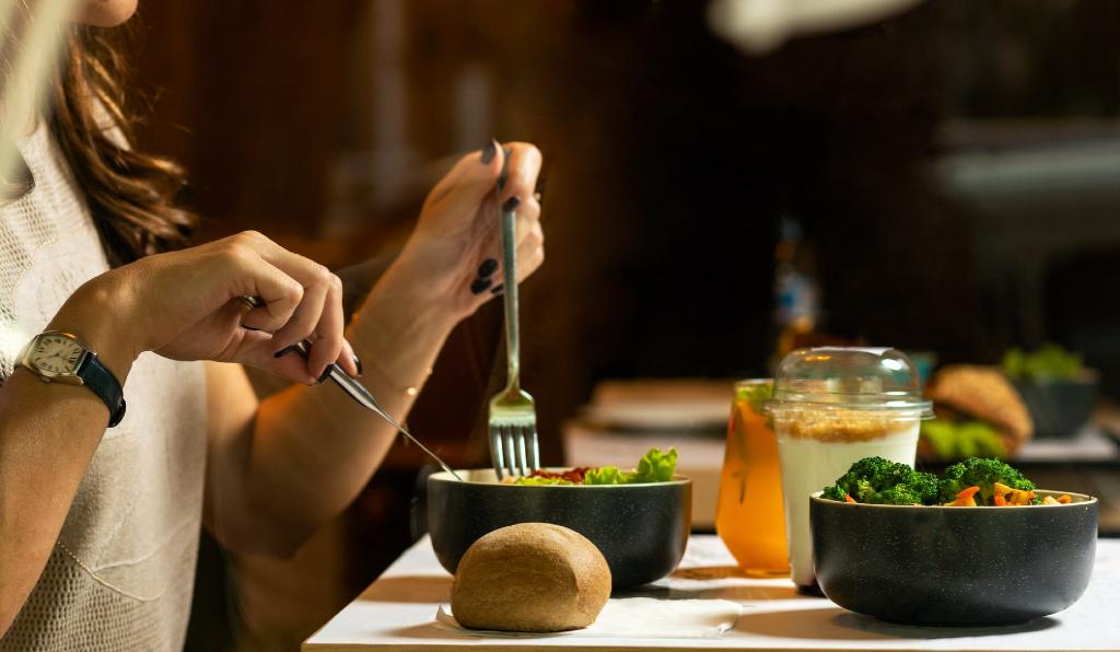 A woman is eating salad, broccoli, and carrots because she wants to banish her banana rolls. 