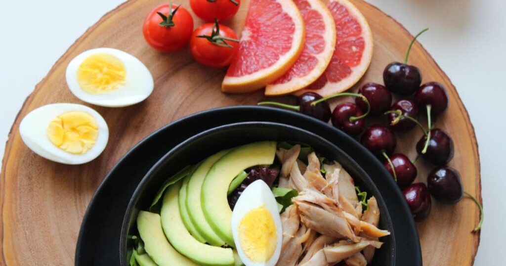 A food platter made for a 500 calorie diet plan contains tomatoes, grapefruits, eggs, avocados, cherries, and chicken.