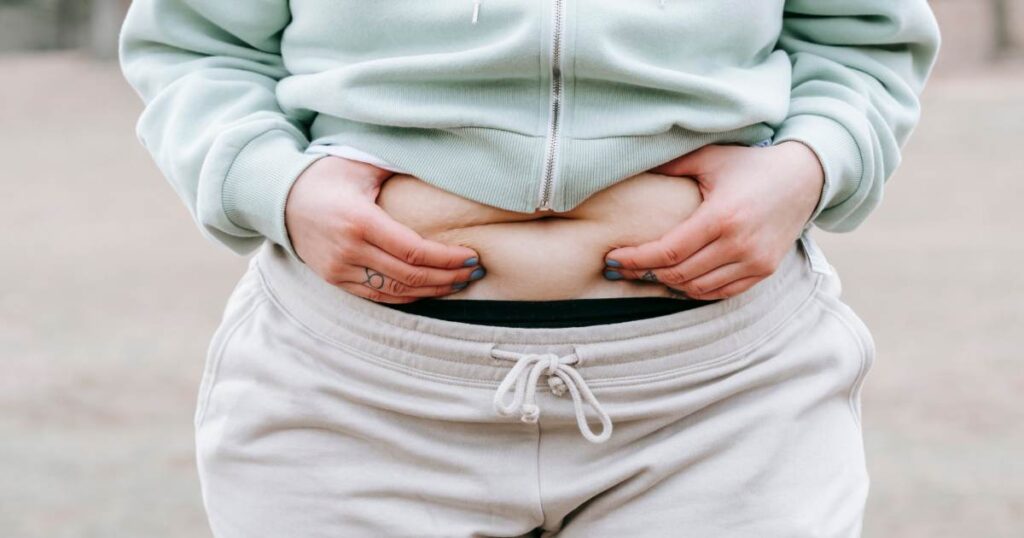 A woman is holding her stomach or jiggly fat while wondering how to get rid of it.