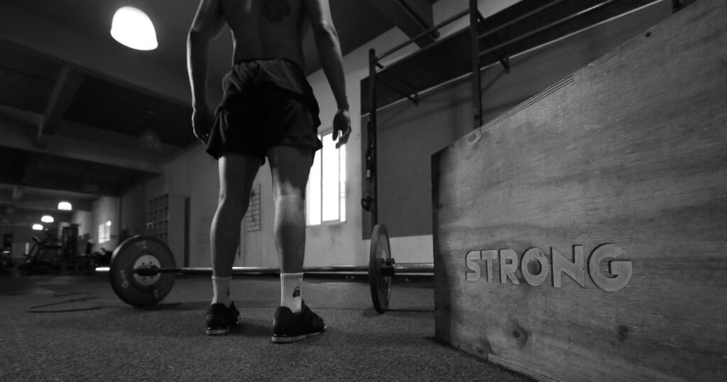 A man is standing in the middle of a gym with a barbell beneath him.