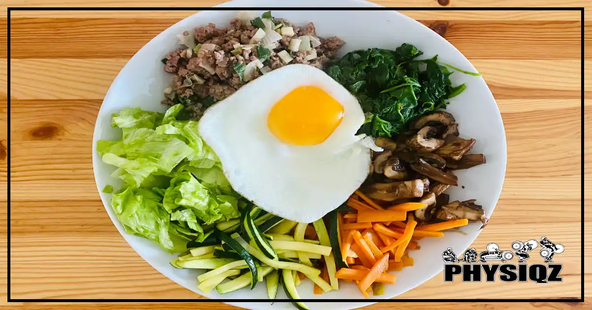 A dish with salad, zucchini, carrots, spinach, mushrooms, beef, eggs and chives as an example of the only meal someone would eat while doing OMAD or one meal a day. 