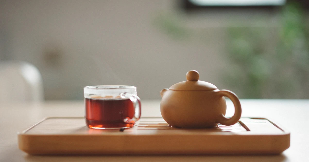 A tea cup and steaming hot cup of tea next to it on a serving plate. 