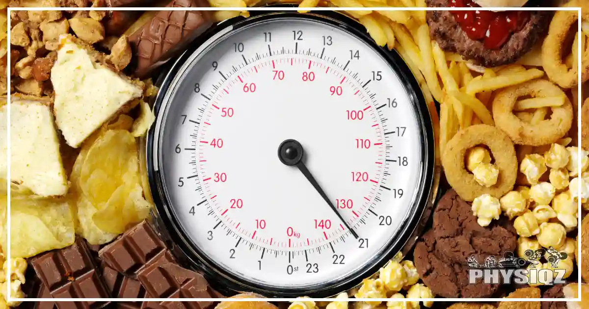 A body weight scale with various junk food around it such as snickers, Hershey milk chocolate, onion rings, cookies chips, and kettle corn. 