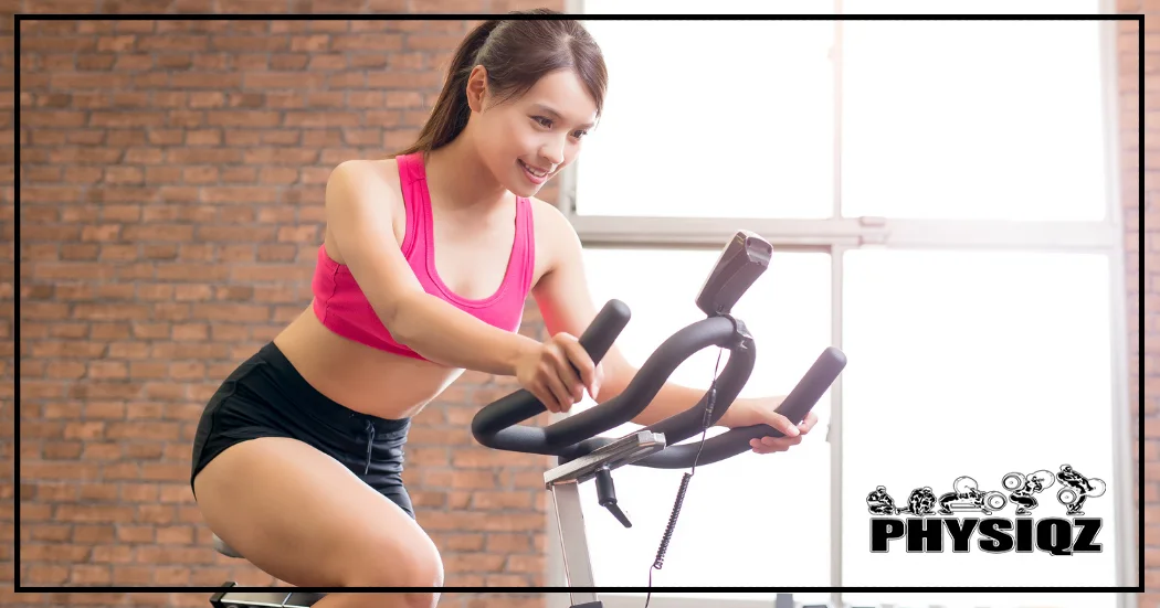 A woman in a pink tank top pedals on a stationary bike against a brick wall, hopeful for one-month results and curious about her body's transformation.