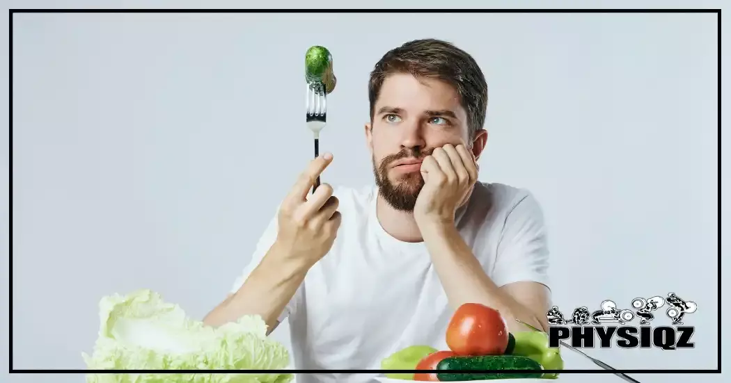 A man is holding a fork that has a cucumber on it with his hand on his chin and lettuce, tomatoes and other veggies sitting below him on a table while wondering if a 1000 calorie deficit diet is worth it.