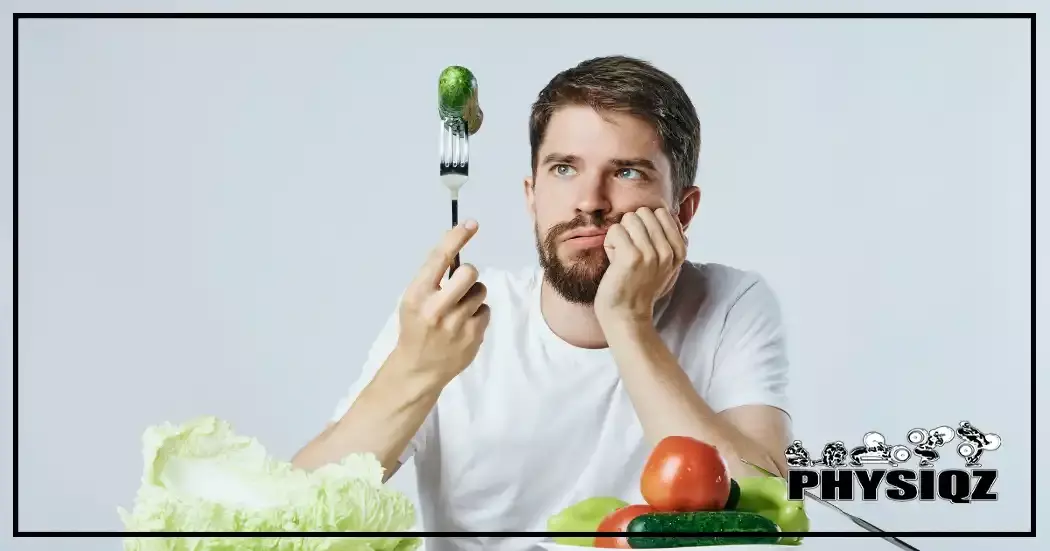 A man holds a fork with a cucumber, his hand on his chin, as he contemplates the value of a 1000-calorie reduction with lettuce, tomatoes, and other veggies on the table below him.