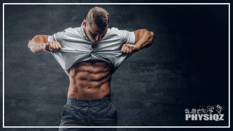 A young, athletic man, dressed in black and white pants, lifts his white shirt to reveal his six-pack abs, gazing at them as he wonders about the quality of his ab genetics.