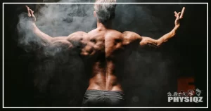 A muscular man posing in a dark room with smoke or chalk in the air asks himself, "How much muscle do you lose on a cut" since he wants to run one more cutting phase.