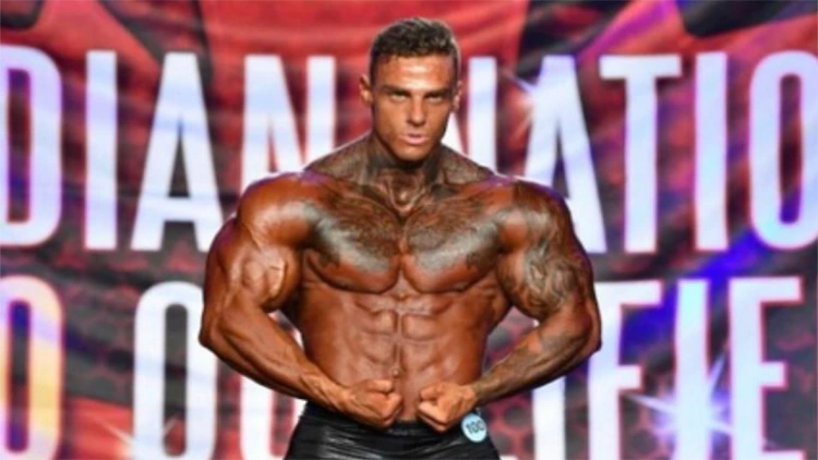 A bodybuilder on stage flexing with his shirt off but his abs are oddly narrow in comparison to his stomach width due to his insertion points. 