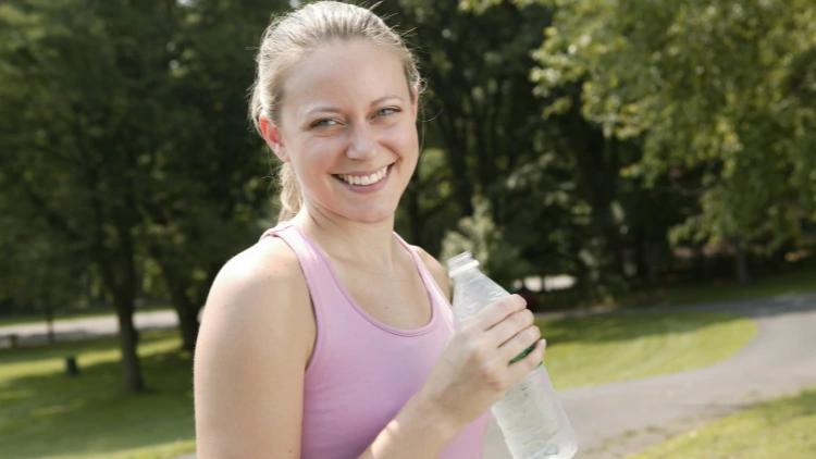 A woman in a light pink tank top poses with a bottle of water in her hand as she's taking a walk in her neighborhood. 