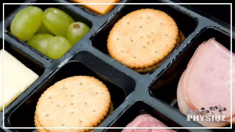 A Lunchables alternative or knock off where it's a black tray that has ham, crackers, cheddar cheese, provolone cheese, and grapes in the tray's slots. 