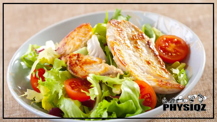 A chicken salad made with romaine lettuce, tomatoes, and chicken on a brown table cloth and in a white salad bowl. 