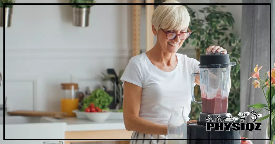 An elderly woman in her 70s is wearing orange glasses and standing in a kitchen while blending up purple vegetable juice while preparing various Grandma home remedies for weight loss.