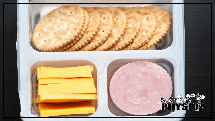 A Lunchable tray that has 3 slots in it, one slot at that has golden brown crackers in it, another at the bottom left with bright yellow cheese and the last slot on the bottom right with round slices of ham where slivers of fat can be seen in white. 