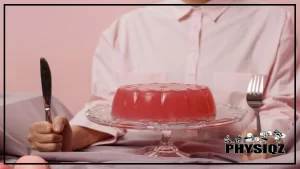 Man wearing a white button-up shirt sits behind a sugar free jello cake with a knife and fork in his hand waiting to eat until he knows how many carbs in sugar free jello are allowed while on a weight loss diet.