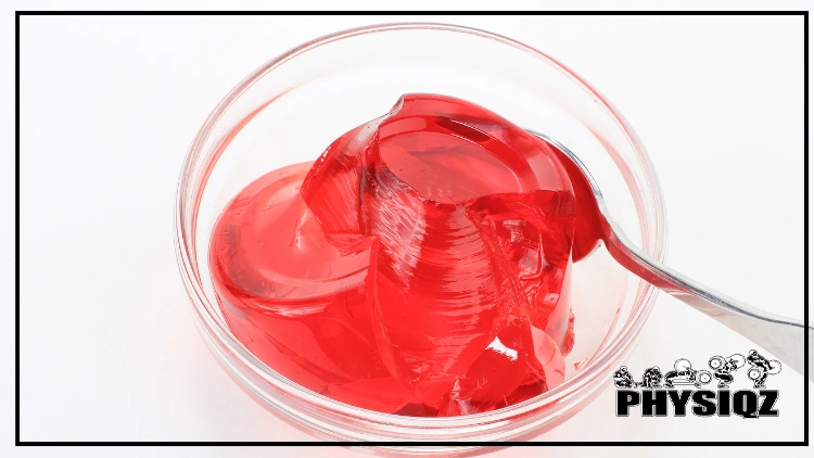 A round glass bowl is holding a dollop of red Jello that has horizontal lines in it and a spoon underneath the glob. 