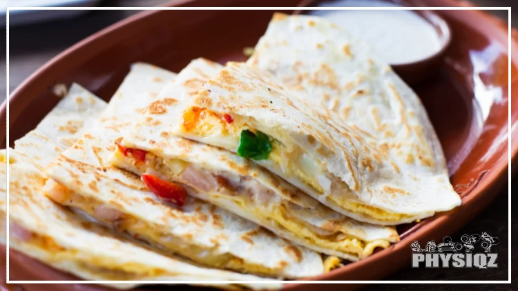A quesadilla filled with cheese, peppers and chicken is cut into four slices that are slightly layered on top of each other and placed in an orange red plate next to a cup of sour cream.