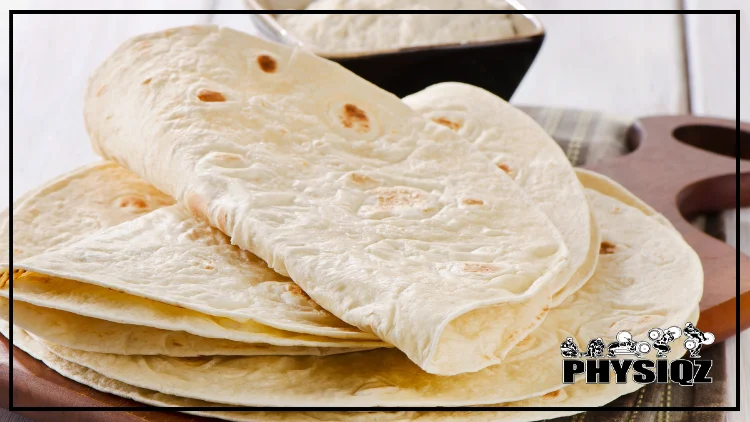 Five flour tortillas are sitting on top of a wooden cutting board and the first three are folded in half.