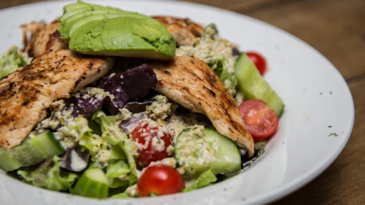 On a white plate, a serving of avocado chicken salad made with ingredients such as avocado, chicken breasts, tomato, and lettuce.