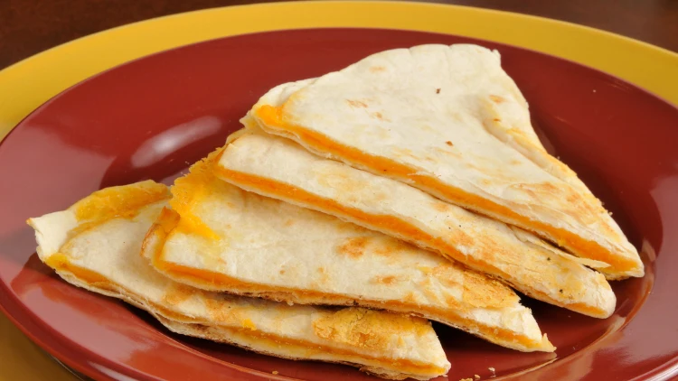 On a red dish, there are four pieces of quesadillas with cheese filling.
