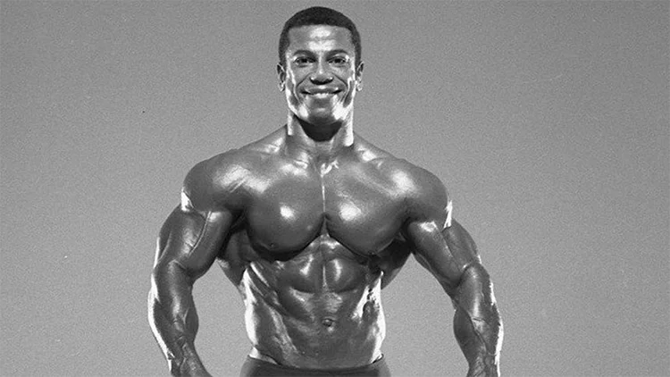 Chris Dickerson is smiling and flexing his entire upper body in a greyscale photo.
