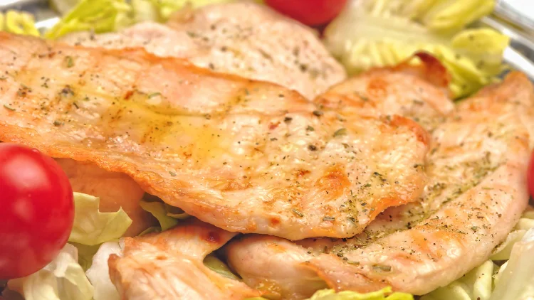 A closeup of a grilled chicken breast with tomatoes and cabbage.