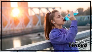 In the background is a blurry cityscape, and the foreground shows a woman in a purple jacket with her hair in a ponytail and listening to music with white earphones as she leans against a city guard rail drinking a blue liquid as she wonders, "Is Vitamin Water keto, or will this knock me out of ketosis?"