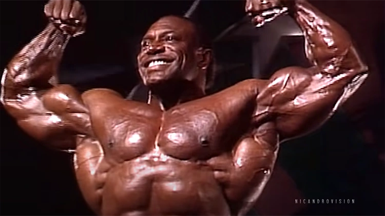 Lee Haney smiling and flexing his muscular arms and showing his chest muscles.