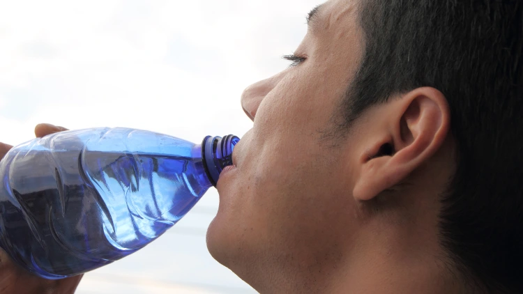 A closeup of a man drinking water from a clear blue plastic water bottle.