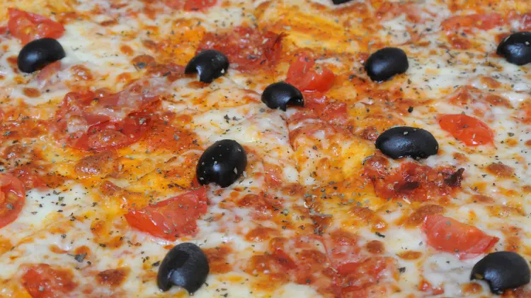 A close-up of a whole pizza with cheese and olives as its toppings.
