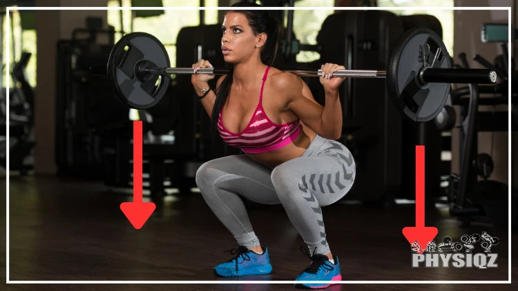 In a gym, a woman wearing a pink sports bra, gray leggings and blue shoes is getting into the bottom of a squat, or in the hole, with a red arrow showing the vertical squat bar path that goes from the barbell to the ground.