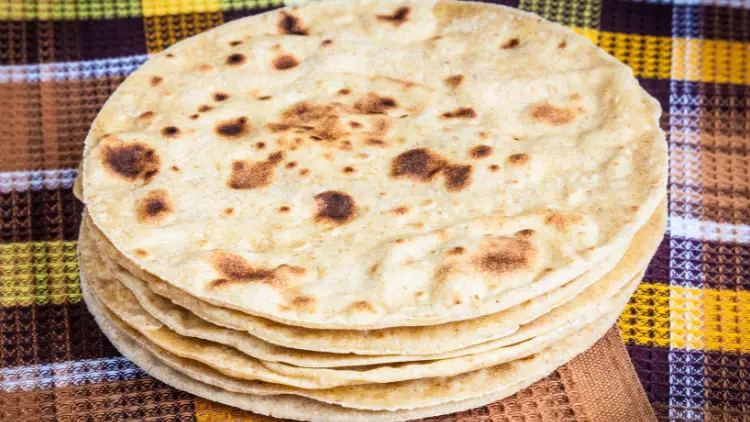 Six thick flour tortillas are stacked on top of a colorful table mat.