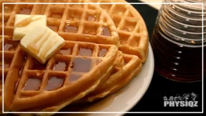 A waffle with butter on top and drizzled with a syrup on a white dish with a syrup bottle beside it that can be ordered from the Waffle House gluten free menu.