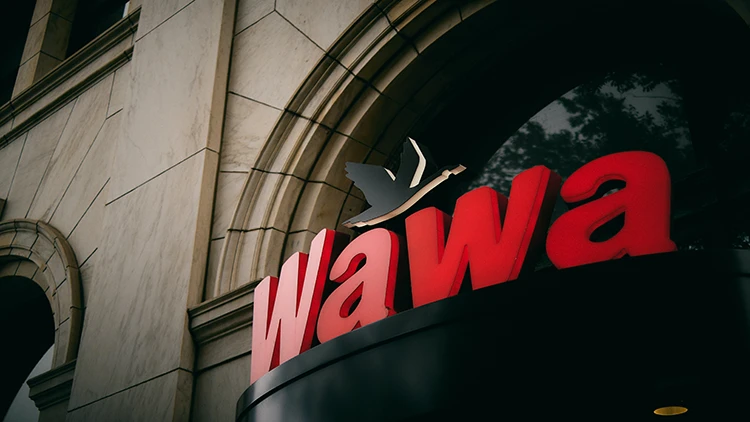 A red sign with the word "Wawa" and a swan above the letters is on top of a black platform of a tan-painted building.
