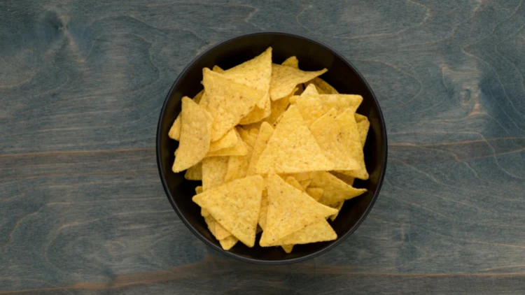 A black bowl filled with tortilla chips displayed on top of a dark-colored wooden surface.