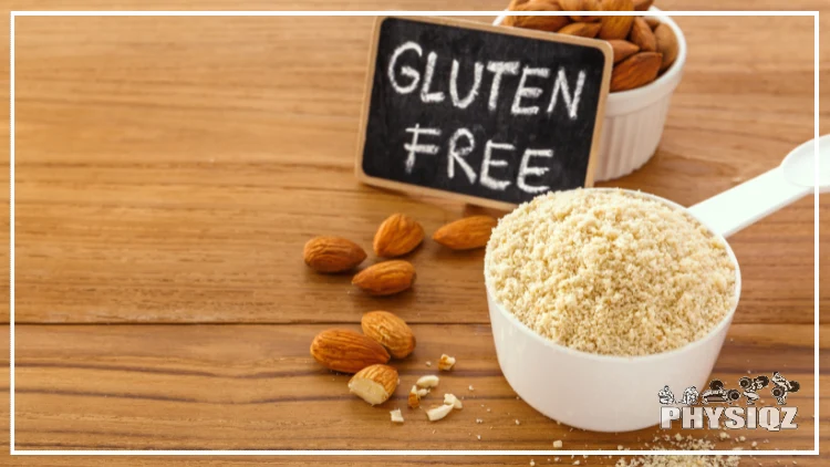 A measuring cup filled with almond flour is sitting next to some almond pieces, a small cup of almonds and a small chalk board that reads "gluten free" on a wooden table. 