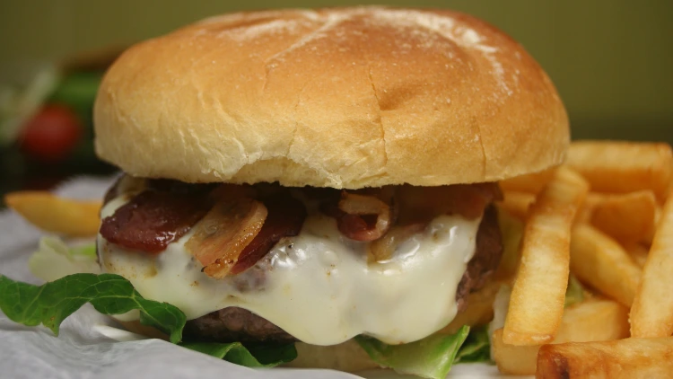 A closeup of a bacon cheeseburger with fries on the side.