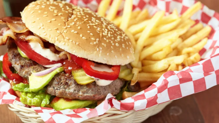 A basket of burger and fries with a red and white wrapper, displayed on top of a wooden surface.